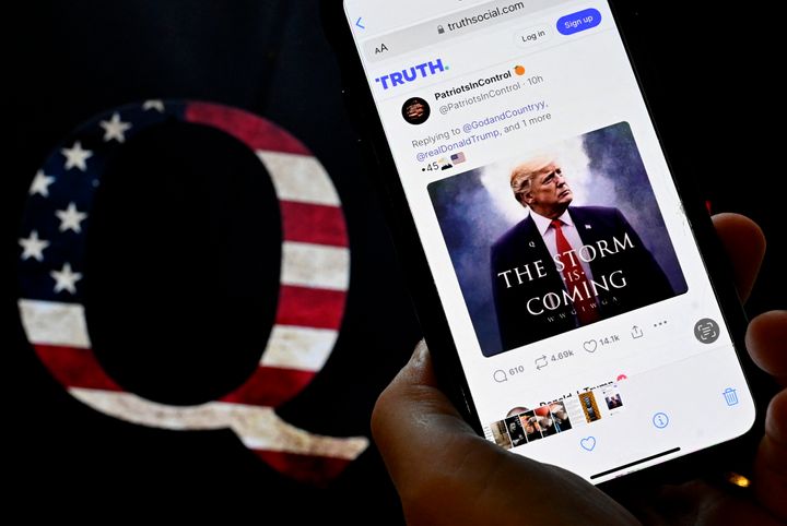 In this photo illustration, Donald Trump's TRUTH Social account is seen on a mobile device with an image of a QAnon sticker in the background in Washington, DC on September 13, 2022. (Photo by OLIVIER DOULIERY / AFP) (Photo by OLIVIER DOULIERY/AFP via Getty Images)