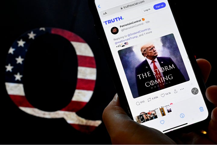 In this photo illustration, Donald Trump's TRUTH Social account is seen on a mobile device with an image of a QAnon sticker in the background in Washington, DC on September 13, 2022. (Photo by OLIVIER DOULIERY / AFP) (Photo by OLIVIER DOULIERY/AFP via Getty Images)