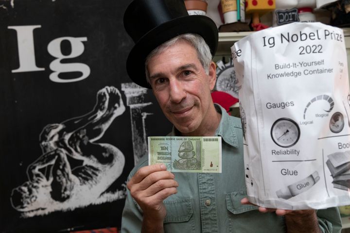 Master of Ceremonies Marc Abrahams poses with the 2022 Ig Nobel prize, as well as a Zimbabwean $10 trillion bill that is part of the prize presented to the winners. (AP Photo/Michael Dwyer)