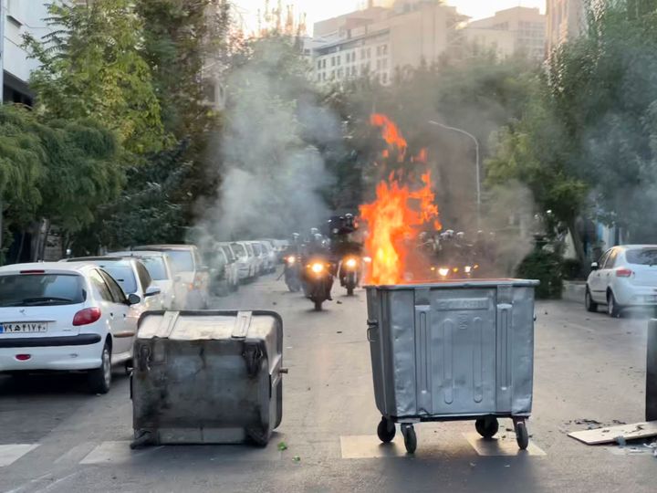 In this Tuesday, Sept. 20, 2022, photo taken by an individual not employed by the Associated Press and obtained by the AP outside Iran, a trash bin burns as anti-riot police arrive during a protest over the death of a young woman who had been detained for violating the country's conservative dress code, in downtown Tehran, Iran. (AP Photo)