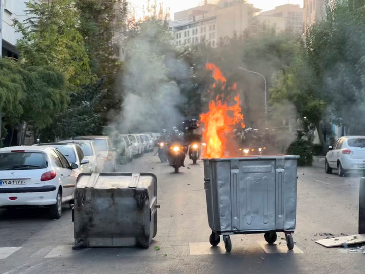 In this Tuesday, Sept. 20, 2022, photo taken by an individual not employed by the Associated Press and obtained by the AP outside Iran, a trash bin burns as anti-riot police arrive during a protest over the death of a young woman who had been detained for violating the country's conservative dress code, in downtown Tehran, Iran. (AP Photo)