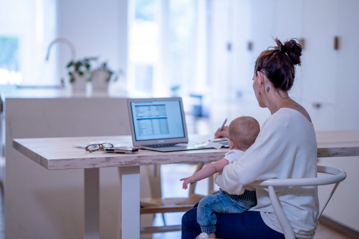 Una mujer trabaja desde casa con su bebé en brazos. FatCamera via Getty Images.