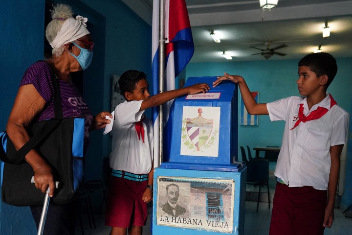 Unos niños ayudan a una mujer a depositar su voto en la urna.