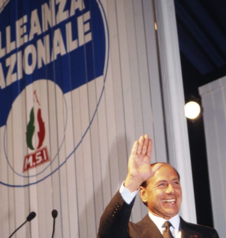 Ο Σίλβιο Μπερλουσκόνι στο συνέδριο της Εθνικής Συμμαχίας το 1995 οπότε και αποφασίστηκε η ένωση του κόμματος με αυτό του ιταλού επιχειρηματία που έμελλε να κυβερνήσει τη χώρα. Πίσω διακρίνεται ξανά το σύμβολο του MSI. 