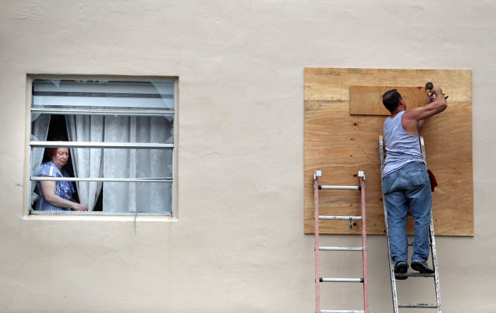 A Kings Point resident looks through her broken window Wednesday as a man boards up another window smashed in an apparent tornado spawned by Hurricane Ian.