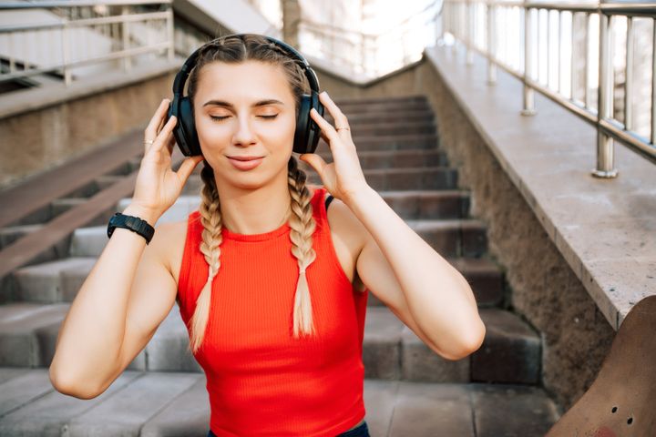 Portrait of woman with wireless black headphones who enjoying and listening music outdoors the street.