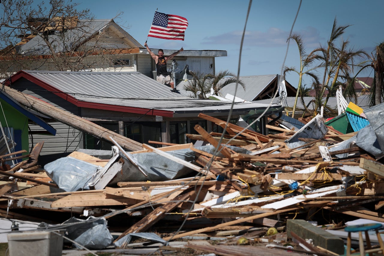 Whitney Hall waves to a friend from the remains of his home while waving the American flag amidst wreckage left in the wake of Hurricane Ian on the island of Matlacha on Sept. 30.