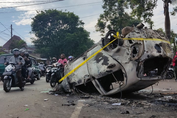 Motorists ride past the wreckage of a car burned during a clash between supporters of two soccer teams, outside Kanjuruhan Stadium in Malang, East Java, Indonesia, Sunday, Oct. 2, 2022. Panic following police actions at the stadium left over 100 dead, mostly trampled to death, police said Sunday.