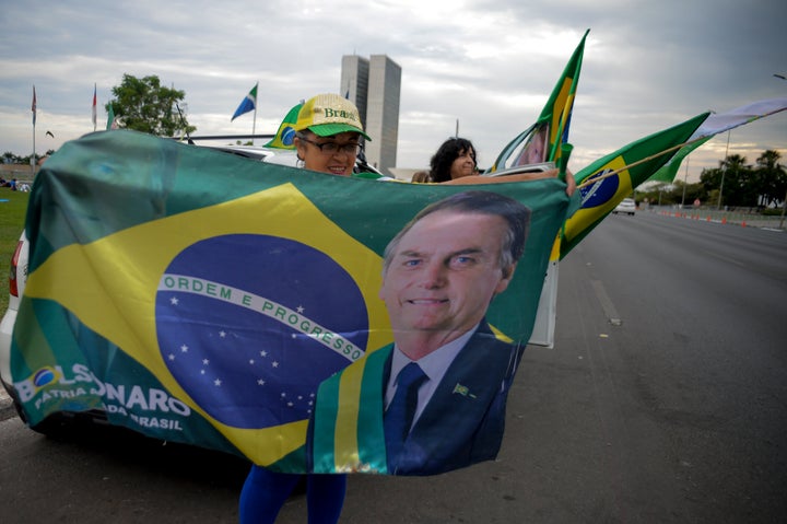 A woman holds a Brazilian flag with the image of Brazilian President Jair Bolsonaro, who is running for another term, after general election polls closed in Brasilia, Brazil, Sunday, Oct. 2, 2022. (AP Photo/Ton Molina)