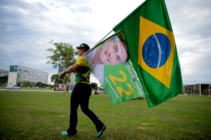 A woman holds a Brazilian flag and another with the image of Brazilian President Jair Bolsonaro, who is running for another term, after general election polls closed in Brasilia, Brazil, Sunday, Oct. 2, 2022.