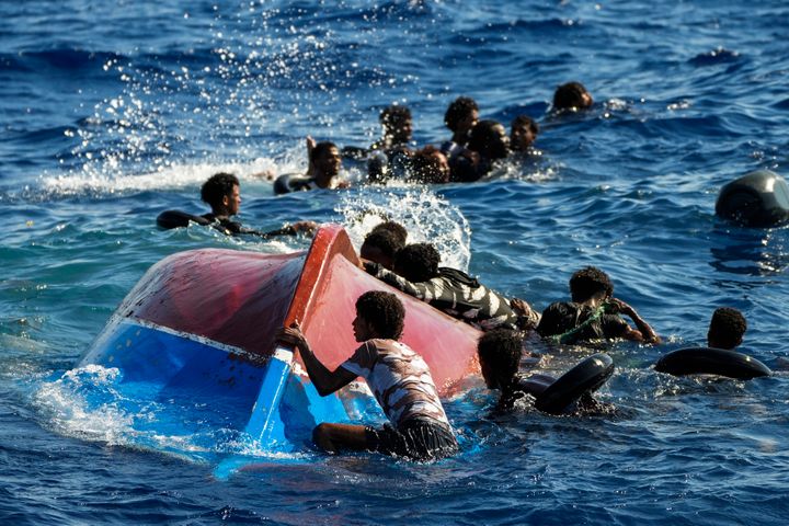 ΑΡΧΕΙΟ - Μετανάστες κολυμπούν δίπλα στην αναποδογυρισμένη ξύλινη βάρκα τους κατά τη διάρκεια επιχείρησης διάσωσης από την ισπανική ΜΚΟ Open Arms στα νότια του νησιού Λαμπεντούζα στη Μεσόγειο, 11 Αυγούστου 2022. (AP Photo/Francisco Seco, file)