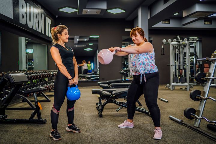 Young female personal trainer working with plus-size woman at a gym