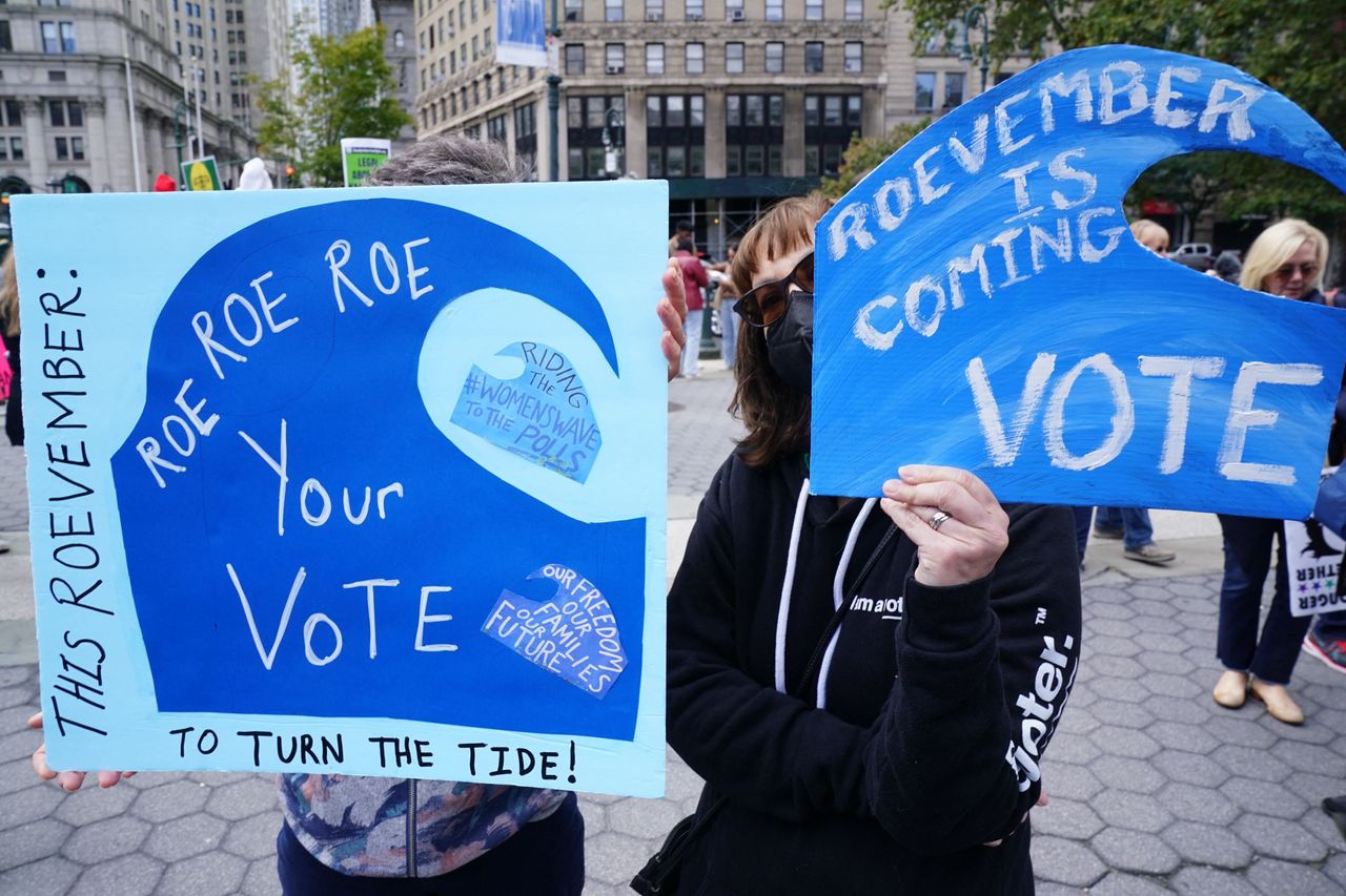 Protesters in New York City hold signs that read: "THIS ROEVEMBER: ROE, ROE, ROE YOUR VOTE TO CHANGE THE TIDE!" Another says: "November is coming.  VOTE"