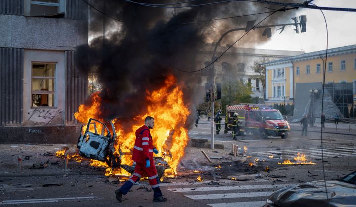 A medical worker runs past a burning car after a Russian attack in Kyiv, Ukraine, Oct. 10, 2022. 