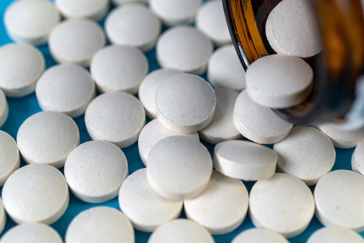 Close-up of medicines spilling from brown a bottle against light blue background.