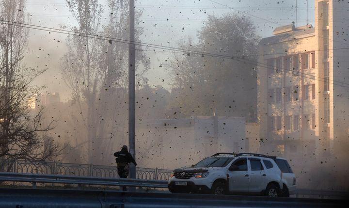 A police officer watches stone and earth debris flying through the air as Russian kamikaze drones hit the centre of the capital Kyiv, Ukraine, on Oct. 17, 2022. 