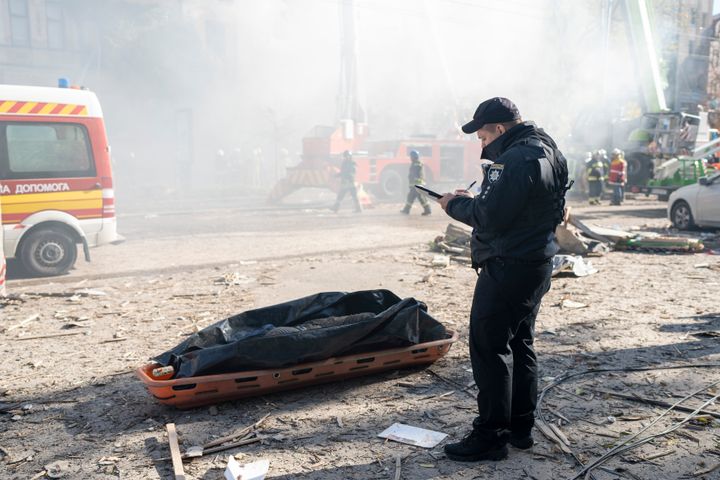 A police officer stands next to the body of a man killed after a drone fired on buildings in Kyiv, Ukraine, on Oct. 17, 2022.