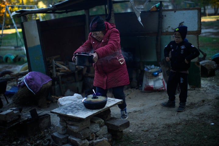 Iryna Panchenko removes a pot of food from a makeshift stove next to her grandchild Artem in Kivsharivka, Ukraine, on Oct. 16, 2022. 