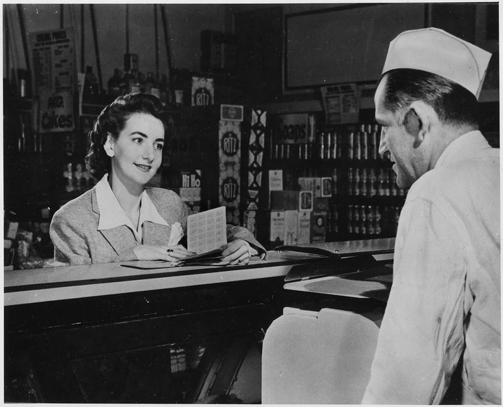 During World War II, a wife and mother presents her ration book to the butcher behind the counter of a deli, Hyde Park, New York, 1943. 