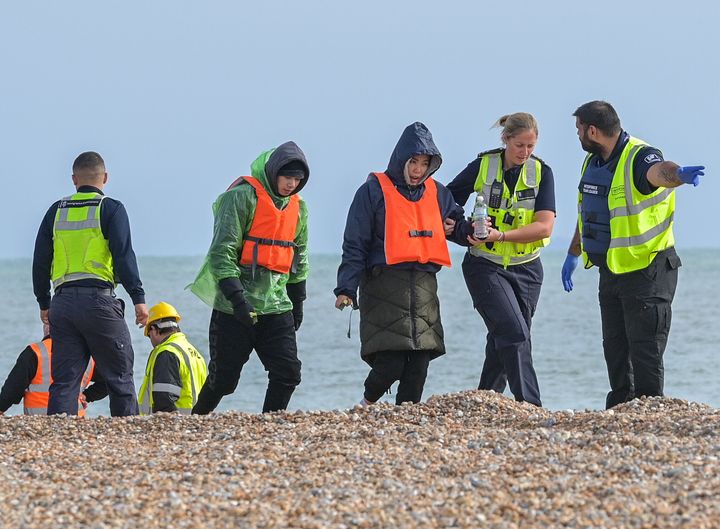 Migrants being helped ashore from a packed lifeboat by the border force and police officers are taken to Dungeness beach in Kent