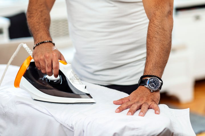 Closeup front view of a males hands with wristwatch and bracelet, ironing white shirt.