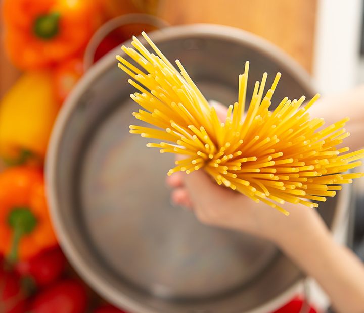 Above view of hand holding a handful of raw pasta noodle in pot in kitchen