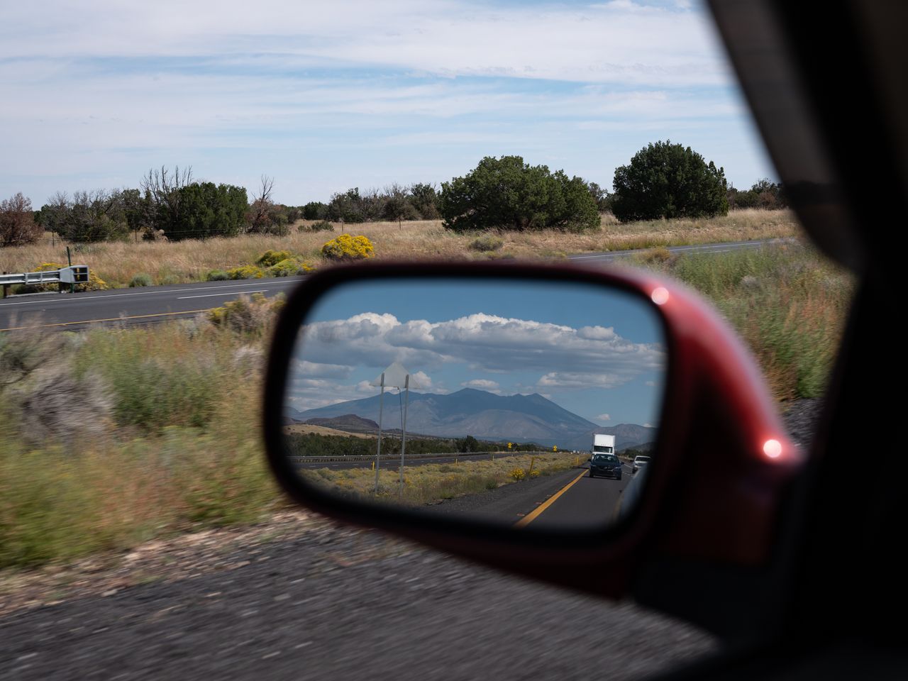 The San Francisco Peaks, mountains sacred to the Diné (Navajo) and other tribes, are reflected in the rearview mirror while traveling east from Flagstaff, Arizona, on Sept. 29, 2022.
