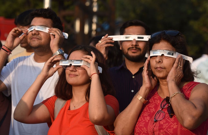 People watch the partial solar eclipse through protective glasses in New Delhi, India.