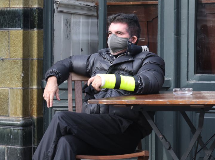 Simon Cowell shows the broken arm he suffered in a bicycle injury as he sits outside The Castle pub in London's Holland Park wearing his cast on 2 February 2022. 