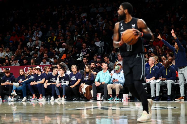 Fans wearing "Fight Antisemitism" T-shirts in the front row look on as Kyrie Irving handles the ball.