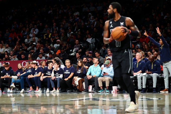 Fans wearing "Fight Antisemitism" T-shirts in the front row look on as Kyrie Irving handles the ball.