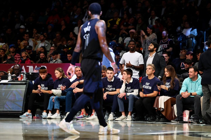 Kyrie Irving walks by fans wearing "Fight Antisemitism" T-shirts during the Nets' game against the Pacers.