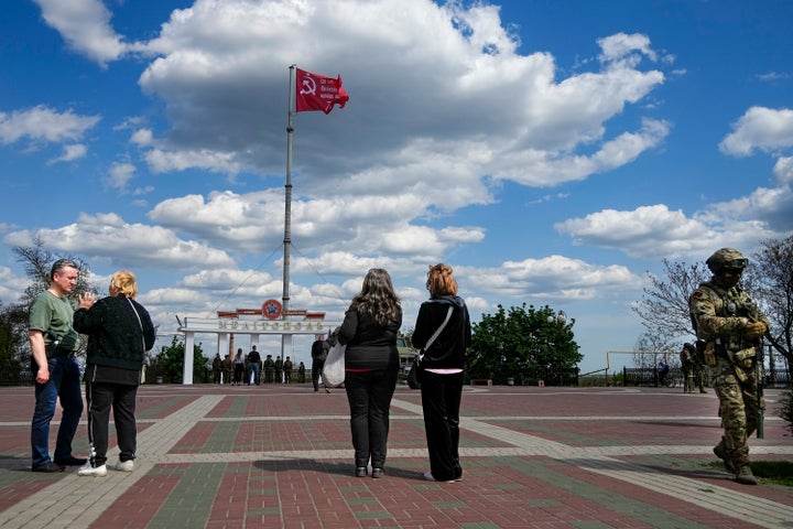 People look as a replica of the Victory banner flutters in the wind over the central square in Melitopol, Zaporizhzhia region, in territory under Russian military control, southeastern Ukraine, on May 1, 2022.