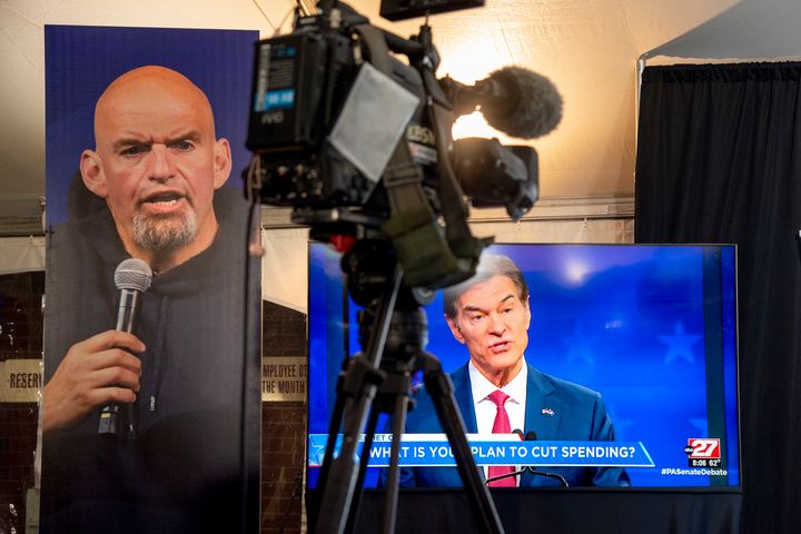 Republican Mehmet Oz, right, is seen live on a monitor in the media tent, next to a poster of Democrat John Fetterman as the two US Senate candidates hold their first and only debate.