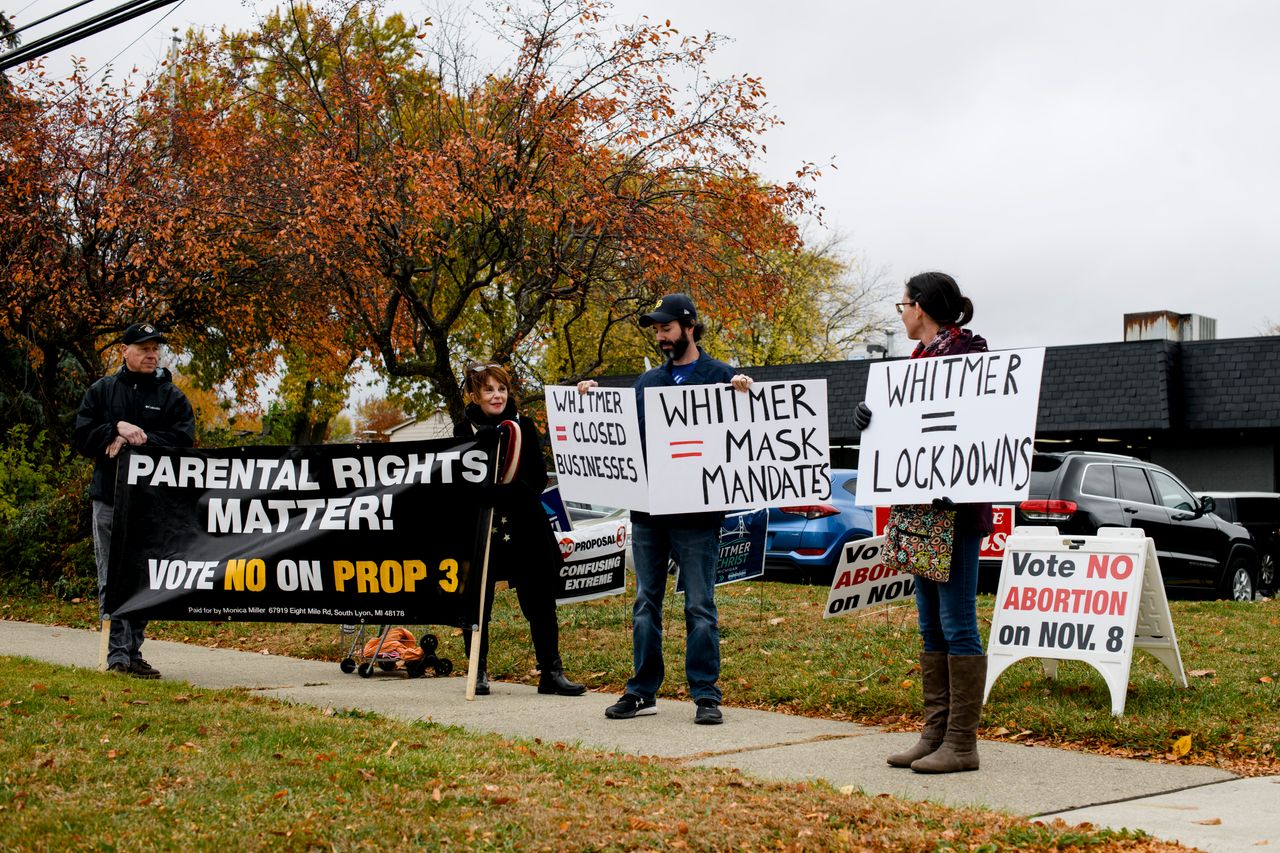 From left to right, A man who wished not to be named, Lynn Mills, a pro-life advocate, Jeff Domsic, of Canton, and Cydney Domsic, of Canton, hold signs in addition to the ones they added to the lawn opposing Whitmer before she was set to arrive at a campaign event in Canton, Michigan, on Oct. 26.