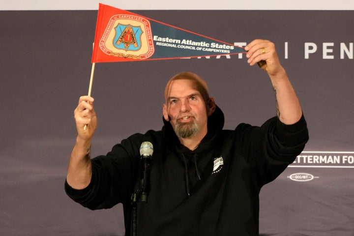 Fetterman holds up an Eastern Atlantic States Regional Council of Carpenters flag as he begins his speech Monday at a Carpenters Union Hall in Pittsburgh.