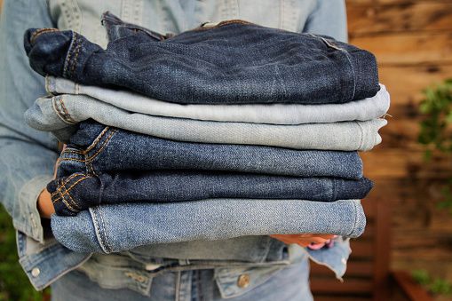 Person holding a stack of folded denim jeans.