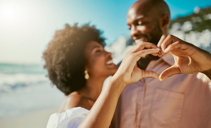 Happy young couple gesturing love enjoying a summer vacation on the beach. Man and woman with love, care and happiness on a romantic getaway. 