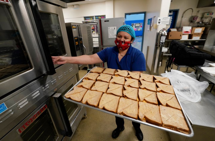 Norma Ordonez places a tray of grilled cheese sandwiches into an oven to warm as she prepares take-away lunches for students kept out of class because of the coronavirus at Richard Castro Elementary School early Friday, Dec. 18, 2020, in west Denver.