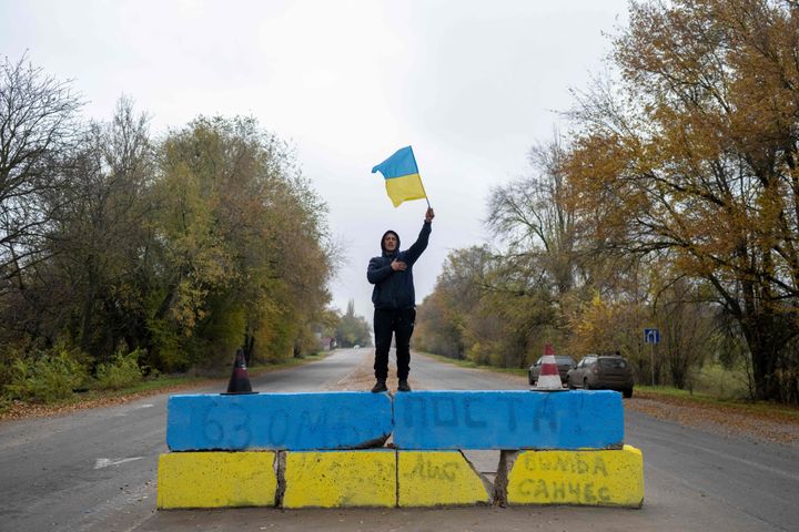 A local resident waves a Ukrainian flag at a former Russian checkpoint at the entrance of Kherson as local residents celebrate the liberation of Kherson