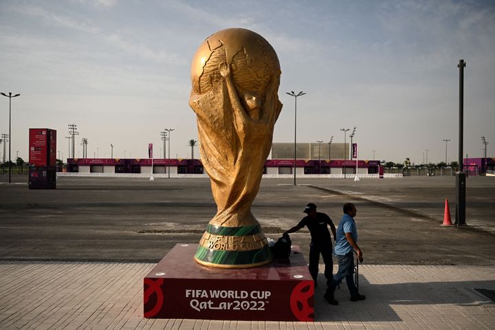 Men walk past a FIFA World Cup trophy replica outside the Ahmed bin Ali Stadium in Al-Rayyan on November 12, 2022.