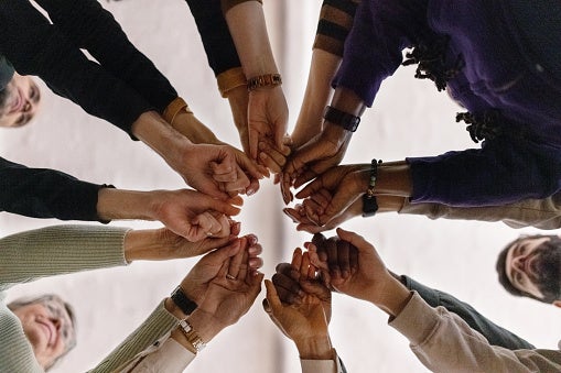 Group of people in circle holding their fists together.