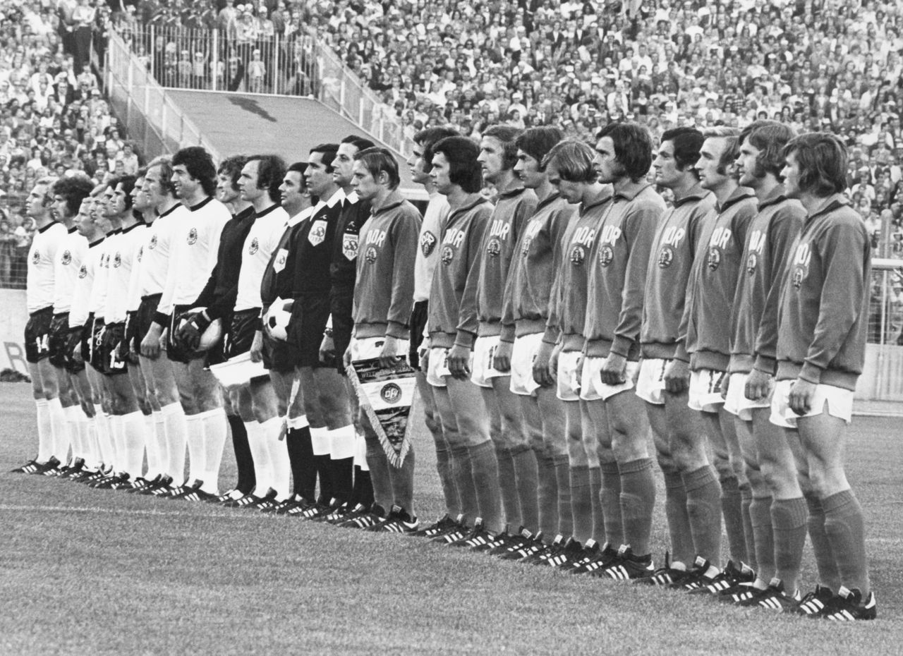Οι ομάδες της Δυτικής Γερμανίας, με τις λευκές φανέλες, και της Ανατολικής Γερμανίας παρατάσσονται στον αγωνιστικό χώρο του Φόλκσπαρκ Στάντιον στο Αμβούργο, για την ανάκρουση των εθνικών ύμνων πριν από την έναρξη του αγώνα, στις 22 Ιουνίου 1974. Το παιχνίδι έληξε 1-0 υπέρ της Ανατολικής Γερμανίας.