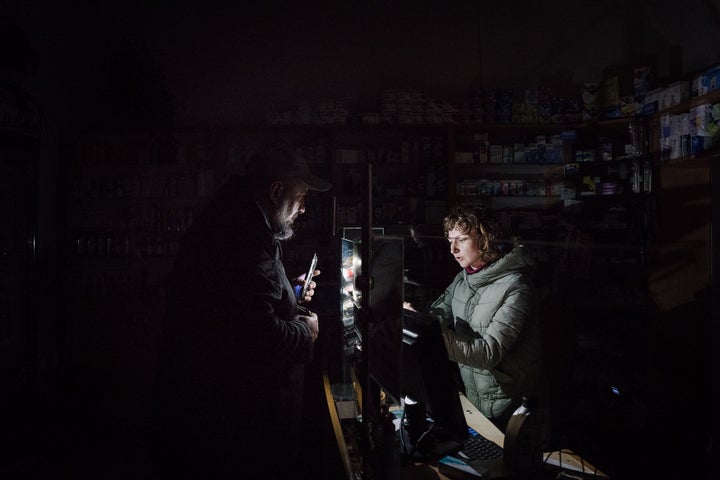 Following the Russian missile strikes on Lviv, the city is experiencing moments of blackout. Here, a customer and a pharmacist try to conduct business by the light of their cellphones.