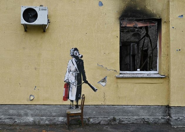 頭にカーラーを巻きながらガスマスクをつけて消化器を持つ女性。ウクライナの首都キーウに近いホストーメリの建物に描かれた（2022年11月16日）
