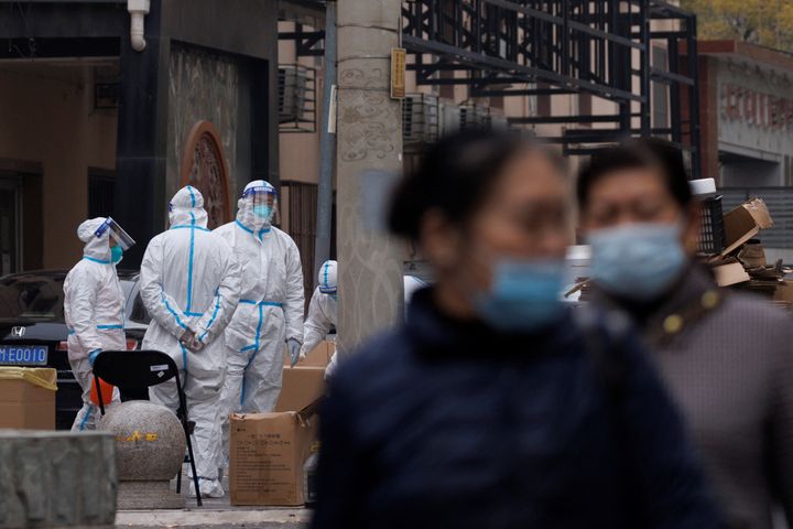 Οι κάτοικοι περπατούν κοντά σε εργαζόμενους για την πρόληψη της πανδημίας με προστατευτικές στολές σε ένα κλειστό οικιστικό συγκρότημα καθώς τα κρούσματα της νόσου του κορονοϊού (COVID-19) συνεχίζονται στο Πεκίνο, Κίνα, 18 Νοεμβρίου 2022.