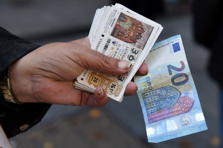 Una persona sostiene en la mano varios décimos de Lotería de Navidad y un billete de 20 euros