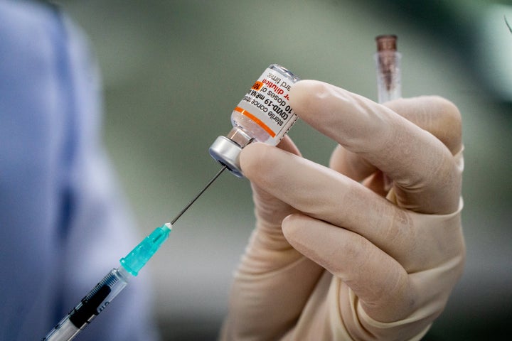 Pfizer-BioNTech COVID-19 vaccine (Comirnaty) doses being prepared by gloved medical worker with syringe