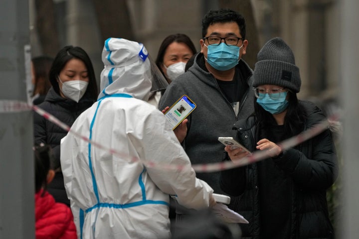 A man shows his health check QR code as he and others line up to get their routine COVID-19 throat swabs at a coronavirus testing site in Beijing, on Nov. 24, 2022.