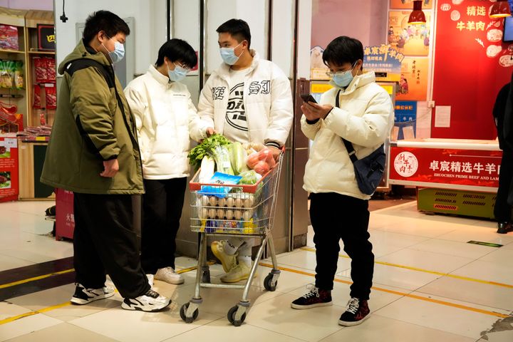 Residents wearing masks wait near a shopping cart of groceries at a supermarket in Beijing, Saturday, Nov. 26, 2022. 